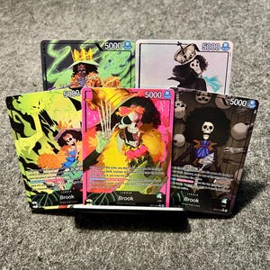Könnte beinhalten: Fünf Sammelkarten mit der Figur Brook von der Strohhut-Crew. Die Karten zeigen Brook in verschiedenen Posen mit leuchtenden Farben, darunter Pink, Grün und Schwarz. Jede Karte hat eine Stärke von 5000.