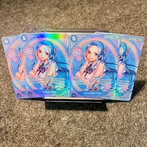 May include: A collection of trading cards, each depicting a character with blue hair and a white dress. The cards feature a blue and pink design, the number "5", and the name "Nefeltari Vivi". They are held in a black card holder.