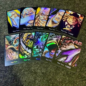 May include: A collection of trading cards featuring various character illustrations. The cards have a black border and include the text "Your Turn" and "+1000". The illustrations showcase detailed artwork with a variety of colors and styles.