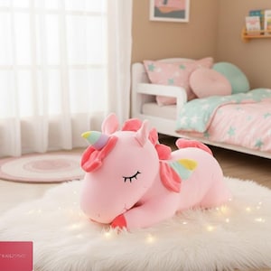 Puede incluir: Un peluche de unicornio rosa con cuerno y alas de arcoíris, tumbado sobre una alfombra blanca y esponjosa. El unicornio tiene los ojos cerrados y está rodeado de una suave iluminación, sugiriendo un dormitorio infantil.