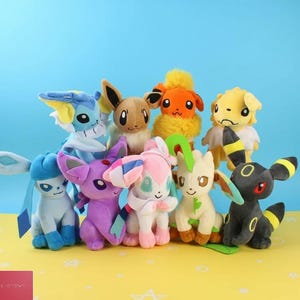 May include: A collection of plush Pokémon figures in various colors, including blue, purple, pink, orange, yellow, and black. The toys have large eyes and detailed features, set against a blue background.
