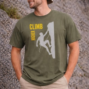 May include: Olive green t-shirt with a graphic of a rock climber and the words "CLIMB HIGHER" in yellow. The climber is depicted in a silhouette, ascending a rock face. The shirt is made of a soft material.