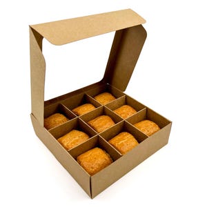 May include: A brown cardboard box with a hinged lid, filled with nine golden-brown pastries. The box is divided into compartments, each holding a pastry. The pastries have a slightly textured surface.