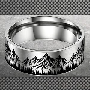 Peut inclure: Une bague argentée ornée d'un motif de chaîne de montagnes. La bande présente une silhouette noire de montagnes et de forêts. La bague a une finition en métal brossé et un intérieur poli. Le design évoque la nature.