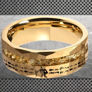 Puede incluir: Anillo dorado con exterior facetado y una banda dorada texturizada. El anillo presenta un patrón repetido de pequeños esqueletos de peces alrededor de la banda. Es una joya.