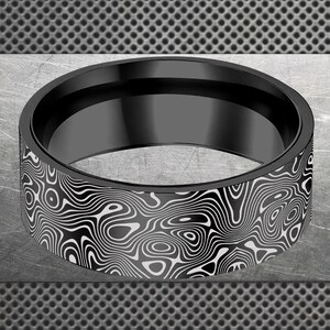 Pode incluir: Um anel preto com um padrão único. O anel tem uma faixa preta e um design detalhado em branco e preto. O padrão assemelha-se a um mapa topográfico ou à textura da madeira. O anel é um acessório arrojado.