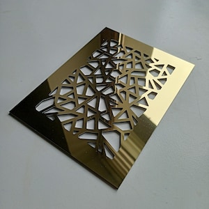 Op de afbeelding: Een rechthoekig, goudkleurig metalen decoratief paneel met een geometrisch, opengewerkt ontwerp. Het patroon bestaat uit onderling verbonden driehoeken en onregelmatige vormen, waardoor een moderne, abstracte esthetiek ontstaat. Het paneel wordt waarschijnlijk gebruikt voor decoratieve doeleinden.