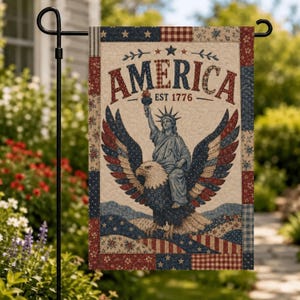 Puede incluir: Una bandera de jardín rectangular con un borde estilo acolchado con patrones en rojo, blanco y azul. El centro muestra el texto AMERICA EST 1776 sobre una ilustración de la Estatua de la Libertad montada sobre un águila calva con alas.