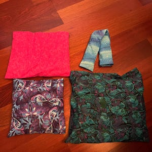 Può includere: Quattro articoli in tessuto sono esposti su una superficie di legno. Un quadrato rosa acceso, una sciarpa a fantasia blu e bianca, un quadrato con un disegno di farfalle viola e un quadrato con un motivo floreale verde.