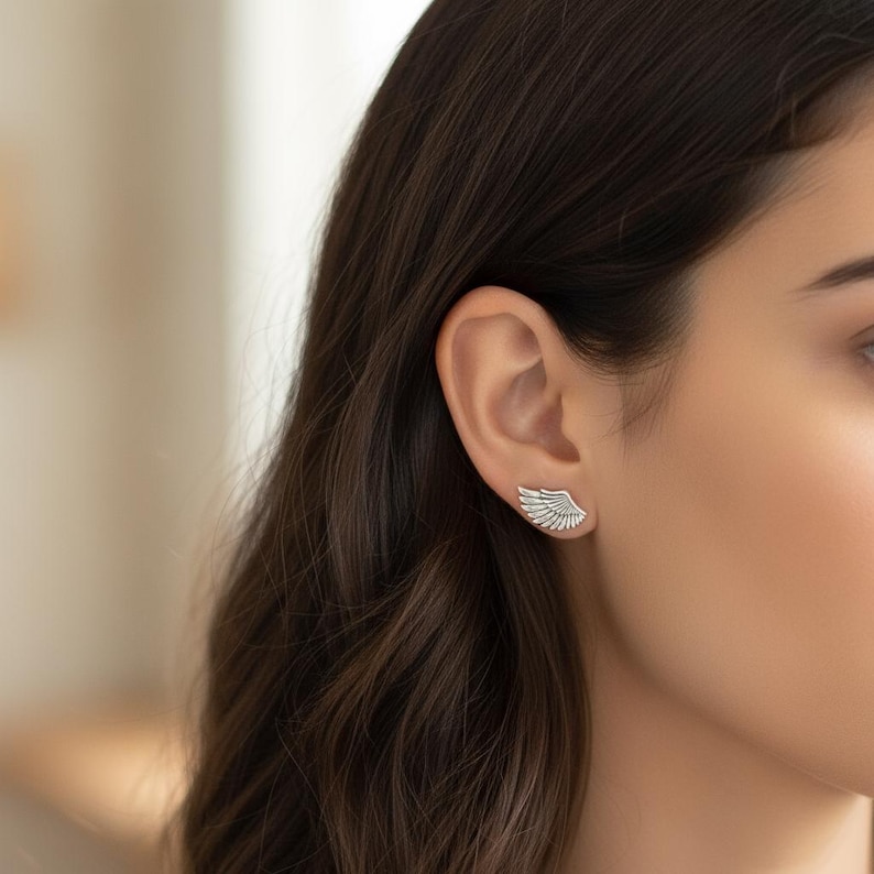 May include: A pair of silver-colored wing-shaped earrings. The earrings are worn on the ear and have a detailed feather design. The earrings are a jewelry item and are likely made of metal.