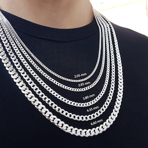 May include: Five silver-toned curb chain necklaces of varying thicknesses, labelled with widths of 2.05 mm, 2.85 mm, 3.80 mm, 4.35 mm, and 6.60 mm. The chains are arranged in a cascading style, showcasing the different link sizes clearly against a dark background.