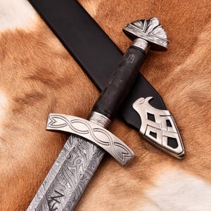 May include: A Viking sword with a patterned blade and silver hilt, lying on a brown and tan fur-like surface. The dark wooden handle contrasts with the silver accents. The sword is accompanied by a black leather sheath.