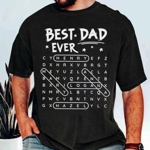 Peut inclure: T-shirt noir avec l'inscription blanche "BEST DAD EVER" et un jeu de mots cachés avec des noms comme Henry, Logan et Hazel. Une idée cadeau personnalisée.