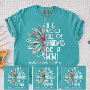 Può includere: T-shirt turchese con un design floreale colorato e la scritta "IN A WORLD FULL OF GRANDMAS BE A MIMI." Include i nomi Sophia, Daniel ed Ethan. Ulteriori design mostrano "NANA", "GRANDMA" e "GIGI."