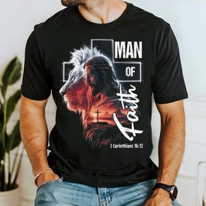 以下が含まれることがあります： 黒いTシャツ。グラフィックデザインには「MAN OF Faith」の文字と聖書の1コリント16:13が含まれています。デザインはライオンの頭とイエス・キリストの描写、背景に十字架が描かれています。