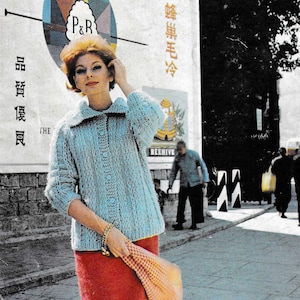 Könnte beinhalten: Eine Frau in einem hellblauen Strickcardigan mit Kragen und Knopfverschluss, kombiniert mit einem roten Rock. Sie hält einen gemusterten Schal. Im Hintergrund befindet sich ein Vintage-Poster.