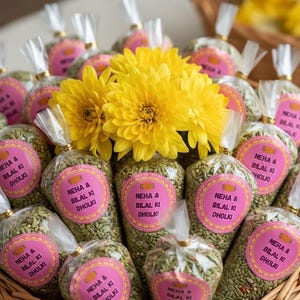 May include: A woven basket filled with cone-shaped packages of seeds, each sealed with a clear wrapper and tied with a ribbon. The packages have pink labels with text. Bright yellow flowers are nestled among the packages.
