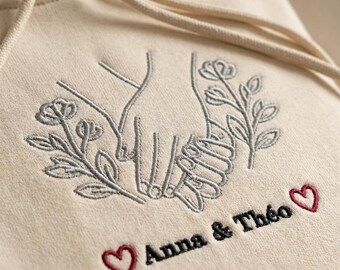 Besticktes Sweatshirt mit ineinander verschlungenen Händen und den Namen des Paares | Geschenk zur Hochzeit, Verlobung oder zum Valentinstag | Handgefertigter Hoodie aus Lille, Frankreich | 22 Farben