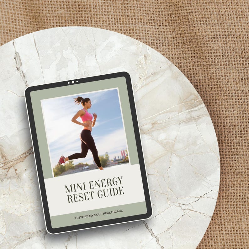 May include: A digital tablet displays a woman running in athletic wear under a blue sky. The tablet's screen features the text "MINI ENERGY RESET GUIDE" and "RESTORE MY SOUL HEALTHCARE". The tablet rests on a marble-like surface, with a burlap background.