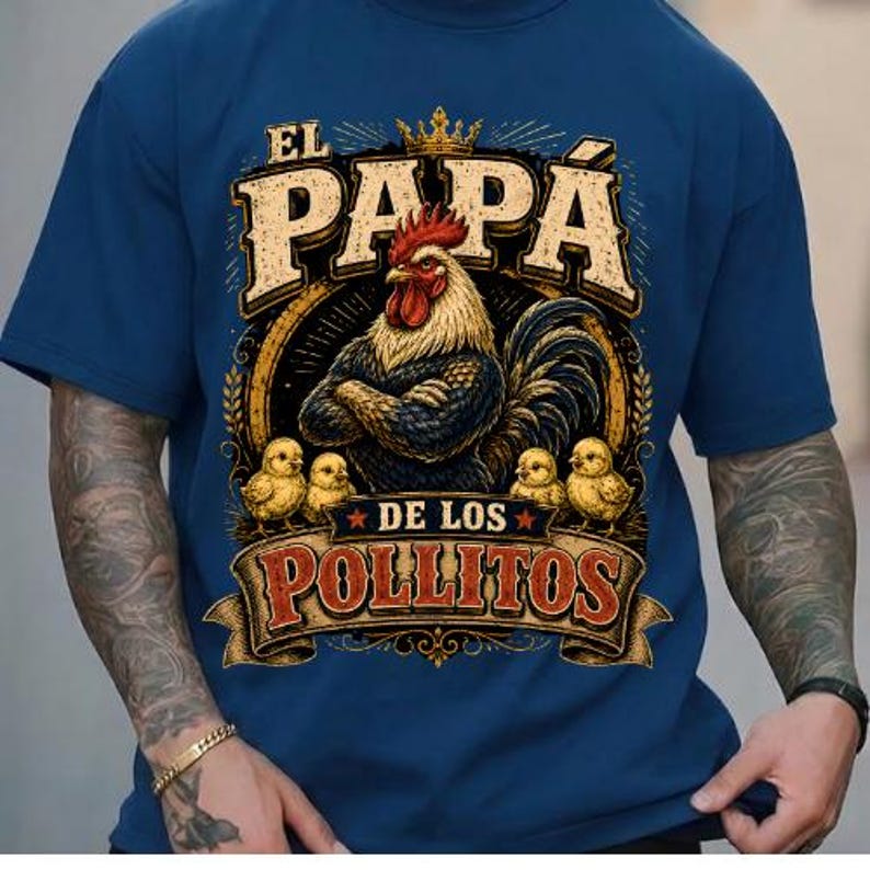 May include: A navy blue t-shirt featuring a graphic print of a rooster with folded wings wearing a crown, surrounded by four small chicks. The text reads EL PAPA DE LOS POLLITOS in a stylized font, with a circular border and decorative elements.