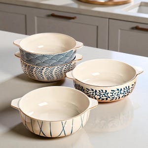 May include: A set of four off-white ceramic bowls with blue and gold accents. Each bowl features a unique blue pattern, including wave, leaf, and geometric designs. The bowls have handles and are suitable for serving.