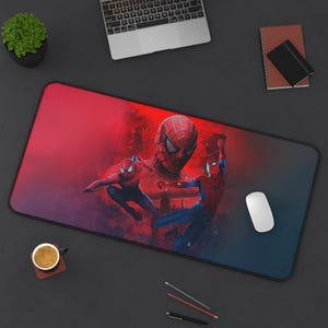May include: A rectangular mouse pad featuring a vibrant image of Spider-Man in action. The design showcases Spider-Man in various poses against a red and blue gradient background. A white computer mouse is on the right.