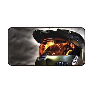 May include: A rectangular mousepad featuring a detailed image of a green and black futuristic helmet with an orange visor. The background is a dark, cloudy sky. The helmet has a sleek, angular design.