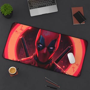 May include: A rectangular mouse pad featuring a vibrant illustration of Deadpool. The design showcases Deadpool's face in a red and black costume, set against a red and orange circular background. Two black katanas are visible. A white mouse and other office supplies are on the dark surface.