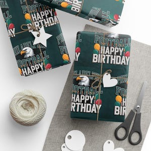 May include: Gift-wrapped presents with dark green paper featuring the text "FOOTBALL HAPPY BIRTHDAY" and a bald eagle graphic. The gifts are tied with twine and adorned with white star and heart-shaped tags. Accessories include scissors and a ball of twine.