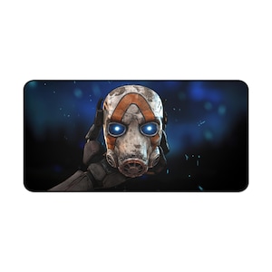May include: A rectangular mousepad featuring a detailed graphic of a character's mask from the video game Borderlands. The mask is primarily white with orange accents and glowing blue eyes. The background is a blurred blue with white specks.