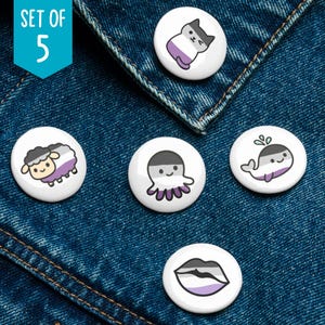 May include: Set of five white round buttons with asexual pride flag designs. Each button features a different cartoon animal or object, including a cat, sheep, octopus, whale, and lips. The buttons are displayed on a blue denim background.
