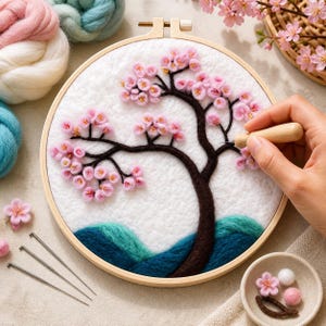 Könnte beinhalten: Ein fertiges Nadel-Filz-Stickrahmen-Kunstwerk mit einem Kirschblütenbaum mit rosa Blüten und einem braunen Stamm. Der Hintergrund ist weiß mit blauen und türkisfarbenen Hügeln. Eine Hand benutzt ein Holzwerkzeug, um an der Kunst zu arbeiten.