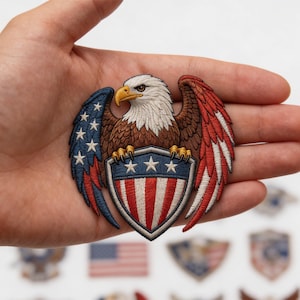May include: Embroidered patch featuring a bald eagle with outstretched wings, a white head, and brown body. The eagle clutches a shield with red and white stripes and blue stars. The wings are red, white, and blue.