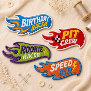 May include: Four embroidered patches shaped like flames with text. One blue patch reads BIRTHDAY RACER, a red patch reads PIT CREW with a checkered flag, a green patch reads ROOKIE RACER with a yellow star, and an orange patch reads SPEED KID.