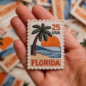 May include: Embroidered patch in the shape of a postage stamp featuring a Florida beach scene with a palm tree, orange sun, and blue ocean. The patch reads "25 USA" and "FLORIDA" in a cream-colored border.
