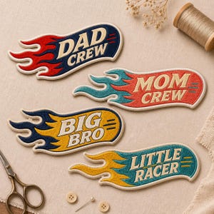 May include: Four embroidered fabric patches shaped like flames. The top patch is dark blue with red flames and reads DAD CREW. The second is red with teal flames and reads MOM CREW. The third is yellow with dark blue flames and reads BIG BRO. The bottom is teal with yellow flames and reads LITTLE RACER.