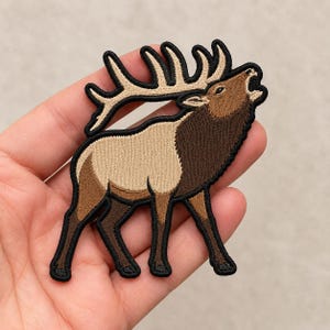 May include: An embroidered patch featuring a bugling elk with large antlers. The elk has a tan body, a dark brown neck and legs, and a black border. The design captures the animal in a vocalizing pose with its head tilted upward and mouth open.