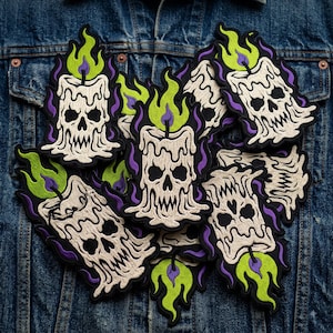 May include: A collection of embroidered patches featuring a melting candle shaped like a skull. The candle is off-white with black eye sockets and a jagged mouth, topped with a bright lime green flame outlined in purple, all set against a dark background.