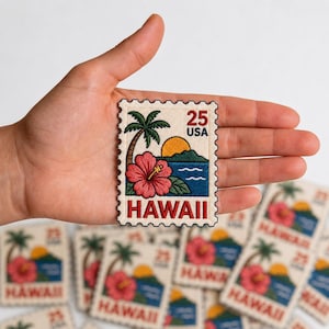 May include: A rectangular embroidered patch shaped like a postage stamp featuring a palm tree, a pink hibiscus flower, a yellow sun, and blue ocean waves. The text 25 USA is at the top right and the word HAWAII is printed in red at the bottom.