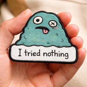 May include: A teal embroidered patch featuring a cartoonish blob with one open eye, a crossed-out eye, and a tongue sticking out. The text "I tried nothing" is embroidered on a white banner below the blob.