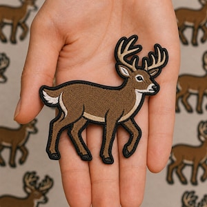 May include: An embroidered iron-on patch shaped like a standing deer with brown fur, a white underbelly, and tan antlers. The patch features a thick black border outlining the entire deer figure, highlighting the detailed stitching and design.