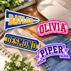 May include: Four embroidered patches featuring names and designs: a blue and yellow triangular pennant with BAYLOR, a pink and white curved patch with OLIVIA, a blue and yellow rectangular patch with DESMOND, and a purple and white banner with PIPER.