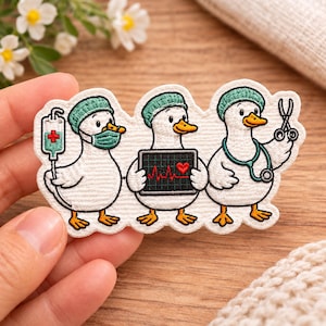 May include: An embroidered patch featuring three white ducks dressed as medical professionals. The first duck wears a surgical cap and mask with an IV bag, the second holds a heart monitor screen, and the third wears a stethoscope and holds scissors.