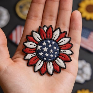 May include: Embroidered patch in the shape of a sunflower, featuring a patriotic design. The center is blue with white stars, surrounded by red and white petals. The patch is approximately 3 inches in diameter.