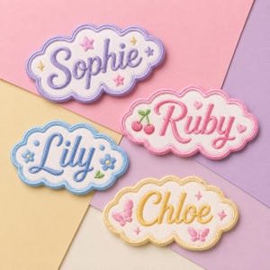 May include: Four cloud-shaped embroidered patches with white centers and colored borders. The patches feature the names Sophie in purple with stars, Ruby in pink with cherries, Lily in blue with flowers, and Chloe in yellow with butterflies.