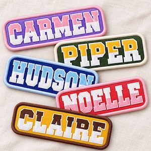 May include: Five rectangular embroidered name patches with rounded corners. The patches feature the names CARMEN, PIPER, HUDSON, NOELLE, and CLAIRE in a bold, block-style font. Each patch displays a two-toned color scheme with white lettering.