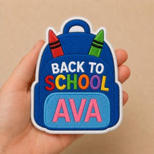 May include: A blue embroidered backpack patch with the text "BACK TO SCHOOL" in white and orange letters. The name "AVA" is in pink letters. The patch has a white border and includes red and green crayon details.