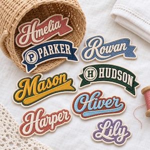 May include: A collection of embroidered name patches in various colors and fonts, including Amelia, Parker, Rowan, Mason, Hudson, Oliver, Harper, and Lily. The patches are shaped like banners or stylized text, featuring white borders and lettering on colored backgrounds.