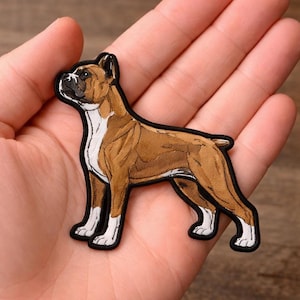 May include: Embroidered patch featuring a Boxer dog in a standing pose. The patch has a brown and white color scheme with black outlining. The dog's features are detailed, and the patch is likely for clothing or accessories.