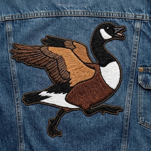 May include: A blue denim jacket featuring a large, detailed embroidered patch of a Canada goose in flight. The goose has a black head and neck, a white throat patch, and wings with shades of brown, tan, and black thread embroidery.